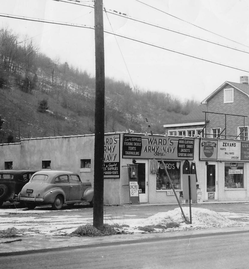 1949 .Vintage black and white photo of a small town street with a store named 'Ward's Army Navy'. Text below the image: A young Hank reports to work for a newly opened Army & Navy store located in Binghamton, NY. Common at the time, A&N stores supplied the public with quality goods from surplus which was generated by the military.