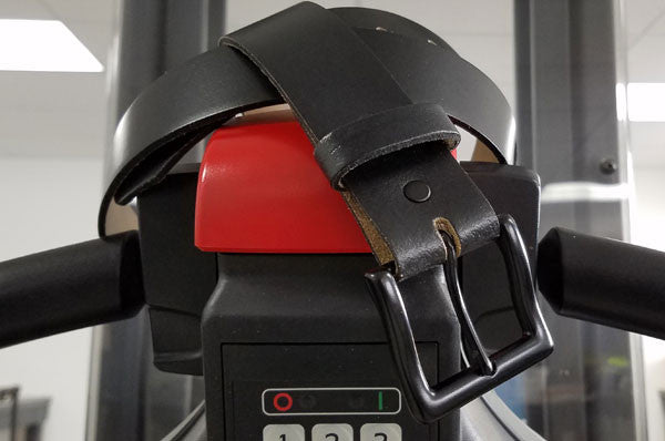 A black leather belt is wrapped and buckled around the display panel of a gym treadmill, covering the red emergency stop button.