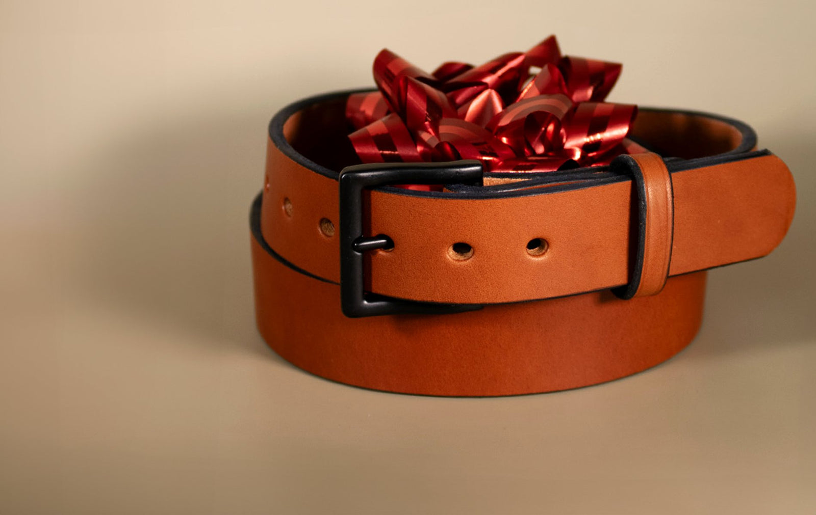 Hanks Everyday belt with red bow on rolled up top on tan backdrop