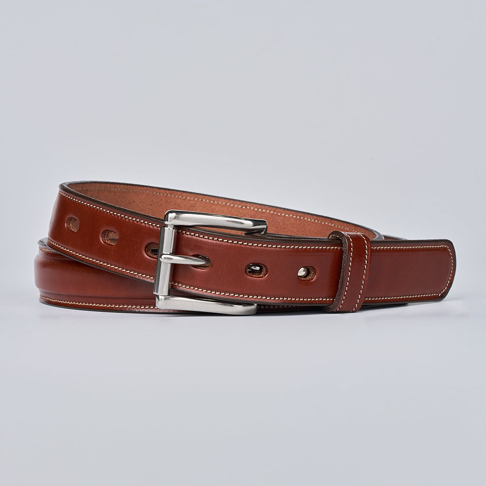 The Esquire Raised by Hanks Belts in Oak, crafted from English Bridle leather with white stitching and a silver buckle, is coiled neatly on a plain light background.